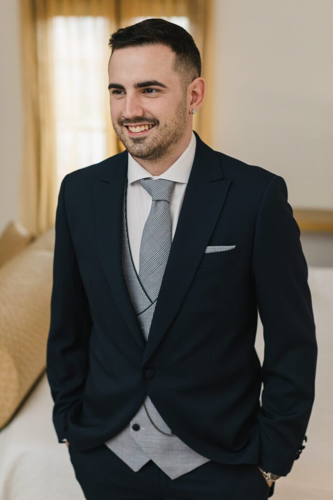 El novio posa para un retrato con una sonrisa radiante, expresando la felicidad y emoción que siente en el día de su boda. Sus ojos brillan con alegría, capturando el amor y la anticipación de este momento especial en su vida.