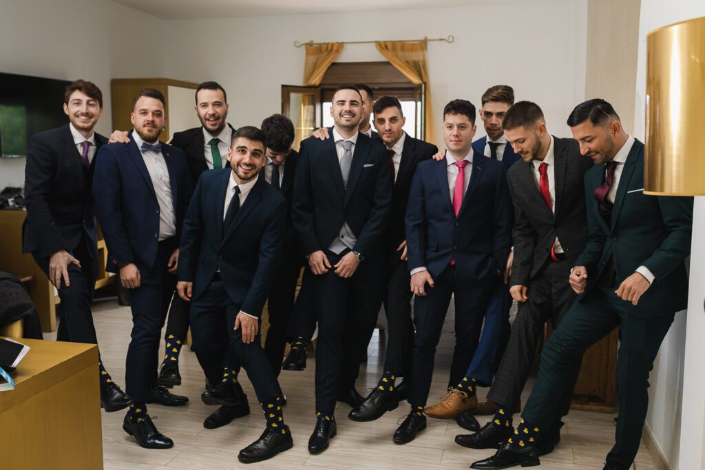 En una divertida sesión fotográfica, el novio y sus amigos muestran los calcetines iguales, levantando un poco los pantalones y compartiendo sonrisas cómplices, creando memorias entrañables juntos.