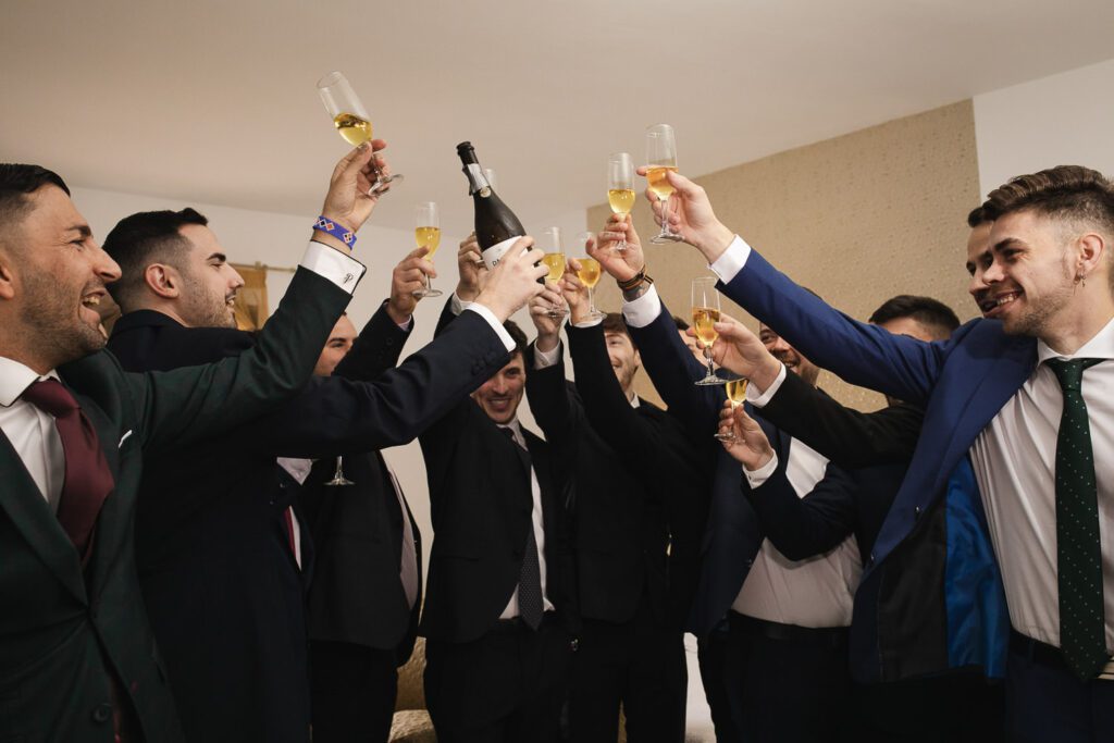 El novio y sus amigos brindan con champagne, capturando un momento de alegría y celebración en una imagen llena de risas y complicidad.